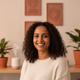 Portrait of a smiling woman in her 30s, looking directly at the camera, with a warm cream and terracotta background.
